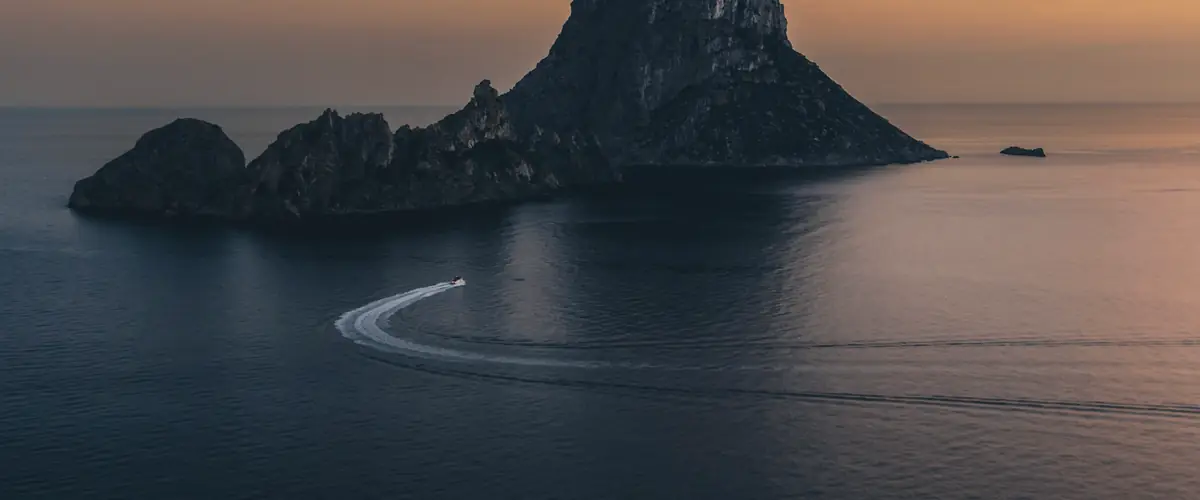 Una lancha deja su estela en el mar frente al islote de Es Vedrà, en Ibiza, al atardecer